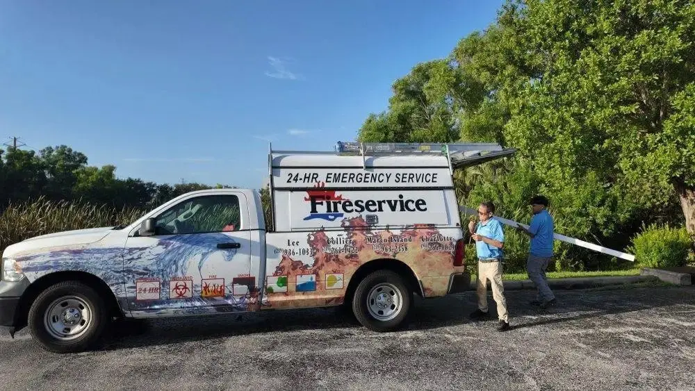 A white emergency service van with a colorful mural is parked on a gravel lot while two people stand beside it.