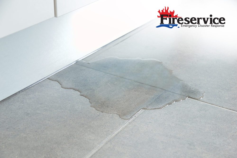 A leak coming from behind cabinets on to a tile floor.